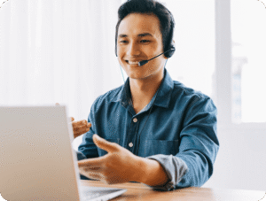 man in headset smiling and gesturing during video call at laptop