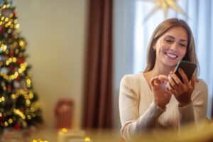 smiling woman texting with christmas tree in background