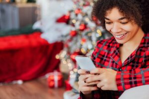 smiling woman texting christmas tree in background